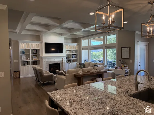 Coffered ceiling with recessed lighting, built-in cabinetry, fireplace with stone surround, large window wall, and wood-finish flooring