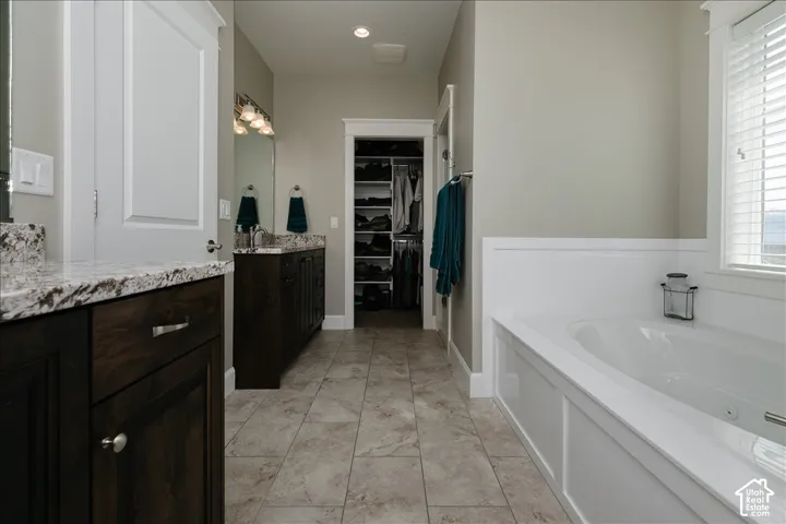 Bathroom featuring a built-in soaking tub, dual vanity with stone countertops, and tile flooring