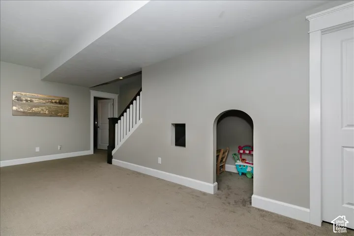Carpeted interior space with a staircase featuring a white spindle railing and dark wood newel post