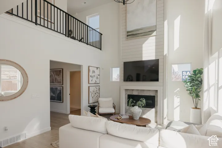 Two-story interior with high ceilings, featuring a gas fireplace with stone surround, wood-finish flooring, a metal railing balcony, and multiple windows