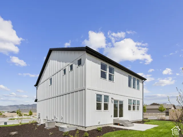 Board and batten exterior with multiple windows, a concrete patio, and a grass lawn
