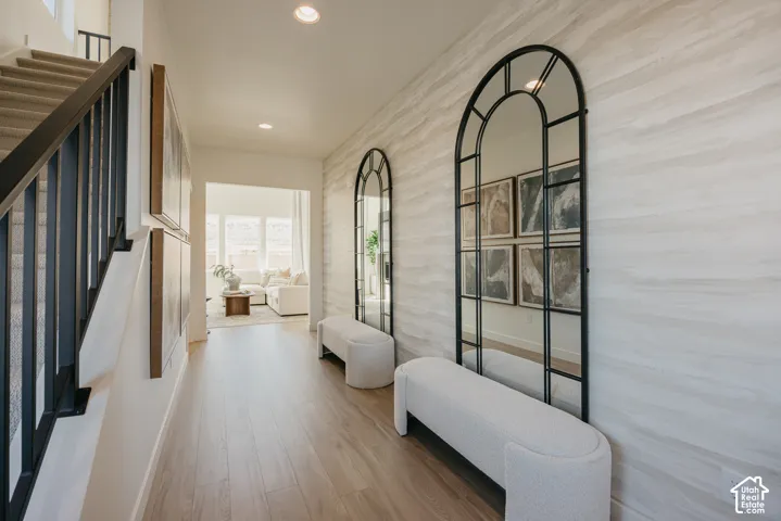 Wood-finish flooring, staircase with dark wood-finish handrail and black metal balusters, textured wall treatment, recessed ceiling lighting, and an arched entryway