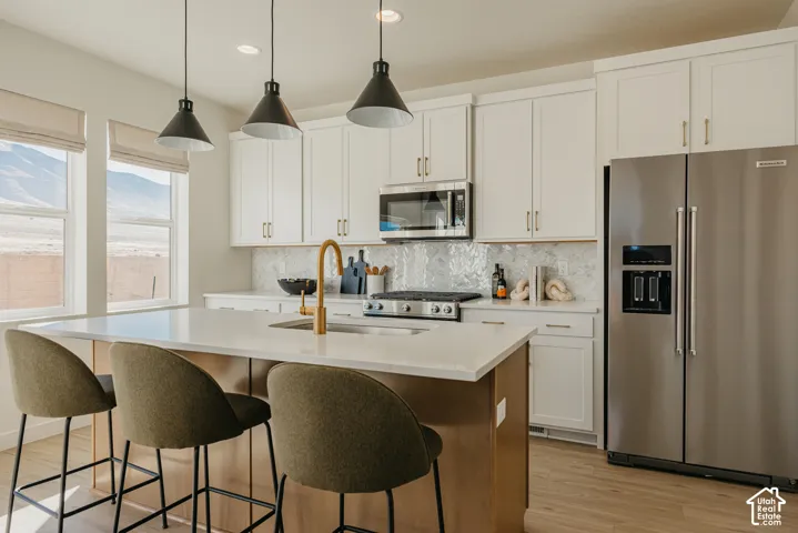 Kitchen featuring stainless steel appliances, white cabinetry, a kitchen island with seating, a gold-finish faucet, and pendant lighting