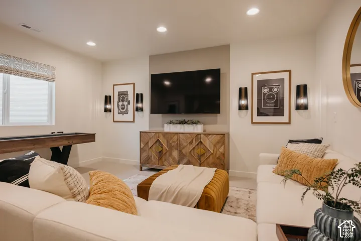 Recessed lighting, wood-finish console with geometric detailing, contemporary wall sconces, large wall-mounted display, and a window with blinds