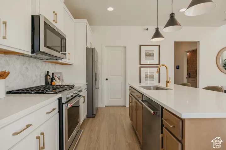 Gourmet kitchen featuring stainless steel appliances, white cabinetry with gold-finish hardware, light wood-finish flooring, and a spacious island with a gold-finish faucet