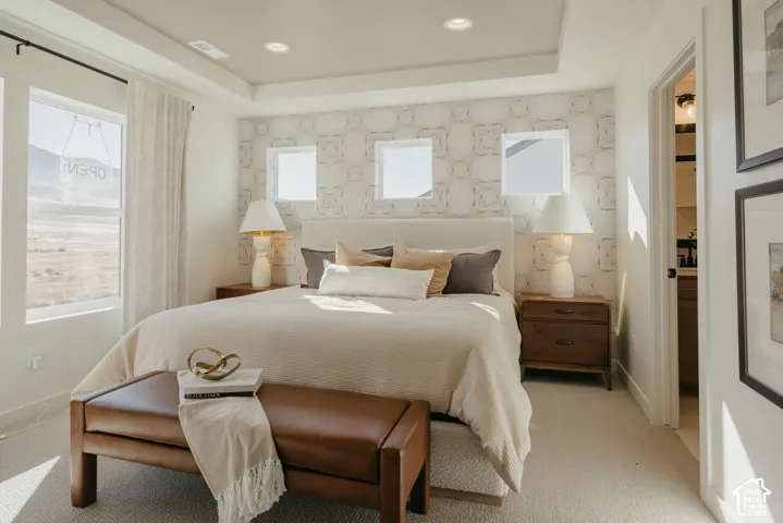 Recessed lighting, tray ceiling, patterned accent wall, large windows, and carpet flooring