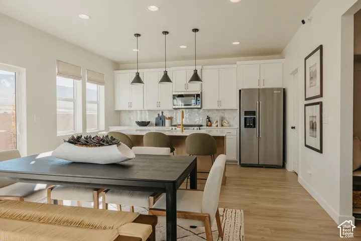 Open-concept dining area and kitchen featuring wood-finish flooring, white cabinetry, recessed lighting, and stainless steel appliances