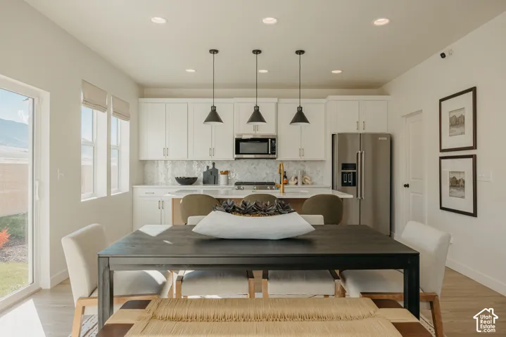 Open-concept kitchen and dining area featuring white cabinetry, stainless steel appliances, and a tiled backsplash