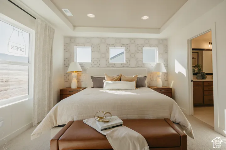 Tray ceiling with recessed lighting, textured accent wall, two large windows, wood-finish nightstands, and a built-in headboard