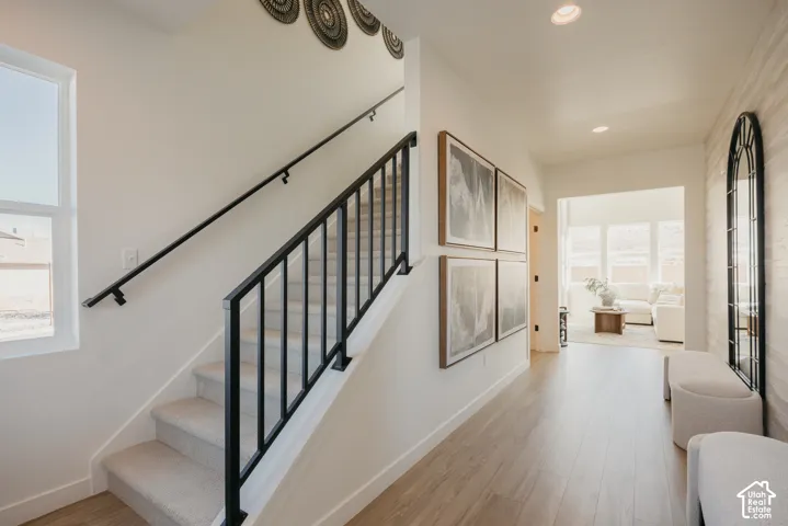 Light wood-finish flooring, recessed ceiling lighting, and a carpeted staircase with black iron railings