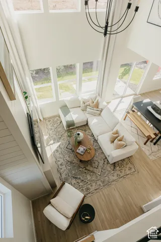 Two-story living area with high ceilings, multiple large windows, a black multi-arm chandelier, and light wood-finish flooring