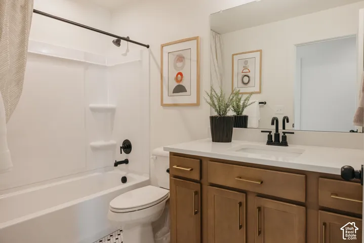Bathtub with integrated shower, single vanity with light wood-finish cabinetry, white countertop, and black hardware