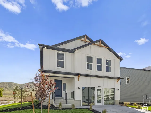 Modern farmhouse exterior with white board and batten siding, black trim, wood rafter tails, a dark entry door, and a concrete driveway