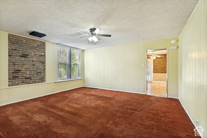 Exposed brick wall detail, multiple windows, built-in ceiling fan, light paneling on walls, carpeted flooring