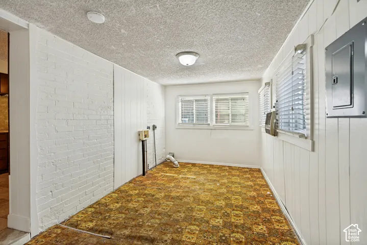 White painted brick wall, wood paneling, multiple windows with blinds, built-in electrical panel, textured ceiling
