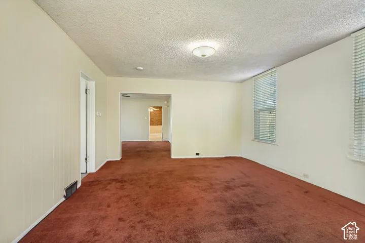Wall-to-wall carpeting in a rich hue, multiple windows providing natural light, and a textured ceiling