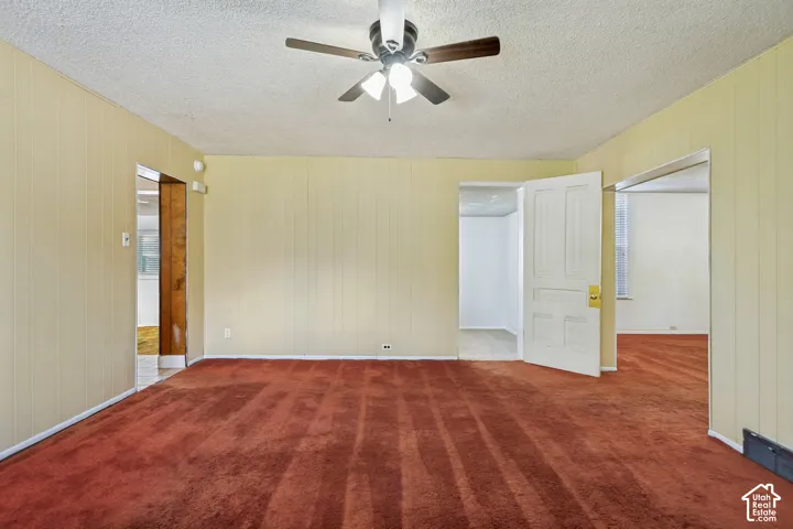 Textured ceiling with a ceiling fan, carpeted flooring, and paneled walls