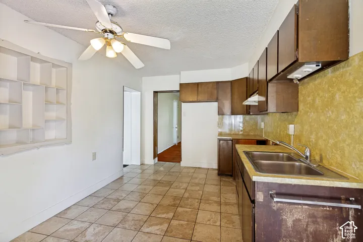 Kitchen featuring tiled flooring, brown cabinetry, a double basin sink, and a built-in recessed shelving unit