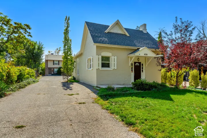 Exterior featuring an asphalt driveway, mature trees, and a peaked roofline