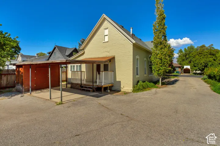 Exterior featuring a light-colored stucco finish, a covered porch with white railings, a detached carport, a separate storage structure, and an asphalt driveway
