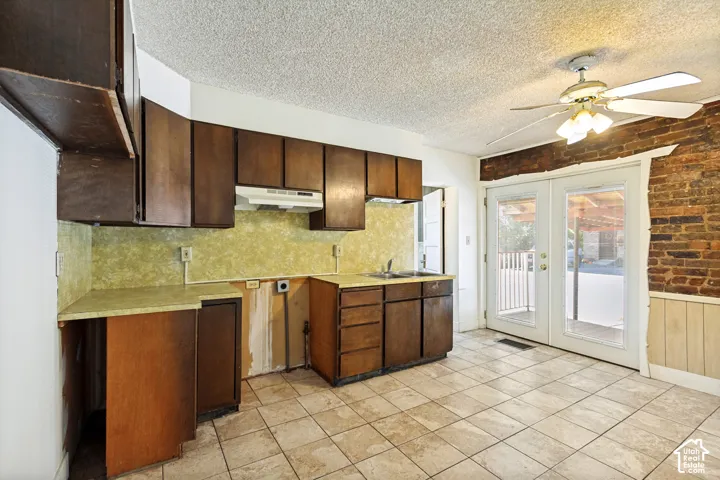 Expansive kitchen featuring wood cabinetry, a built-in range hood, a stainless steel sink, and light-toned tile flooring