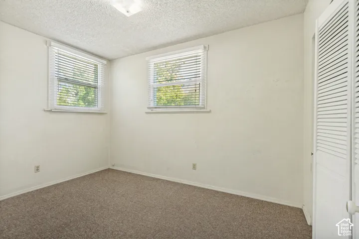 Carpeted room with two windows, horizontal blinds, and a louvered bi-fold closet door