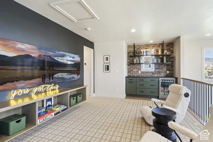 Built-in media console with open shelving, integrated wet bar featuring brick-look tile backsplash, green cabinetry, and beverage refrigerator, and patterned carpeting