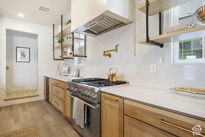 Gourmet kitchen with light wood-finish cabinetry, stainless steel range, light quartz countertops, and open shelving