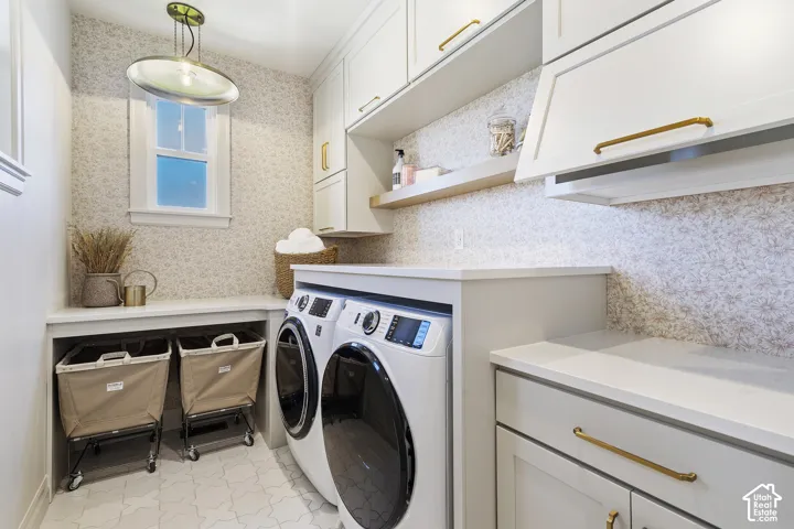 Built-in cabinetry with gold-finish hardware, light-toned countertop surfaces, window with natural light, patterned wall covering, and tiled flooring