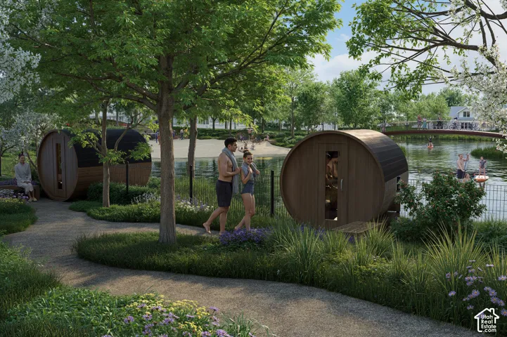 Manicured landscaping with a paved pathway, two cylindrical sauna structures, and a body of water