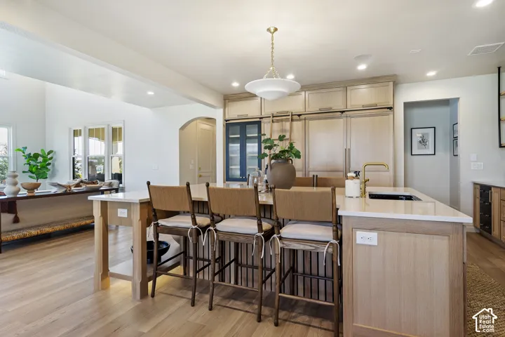 Spacious kitchen featuring a large central island with seating, built-in sink with a gold-finish faucet, integrated paneled appliances, and ample cabinetry