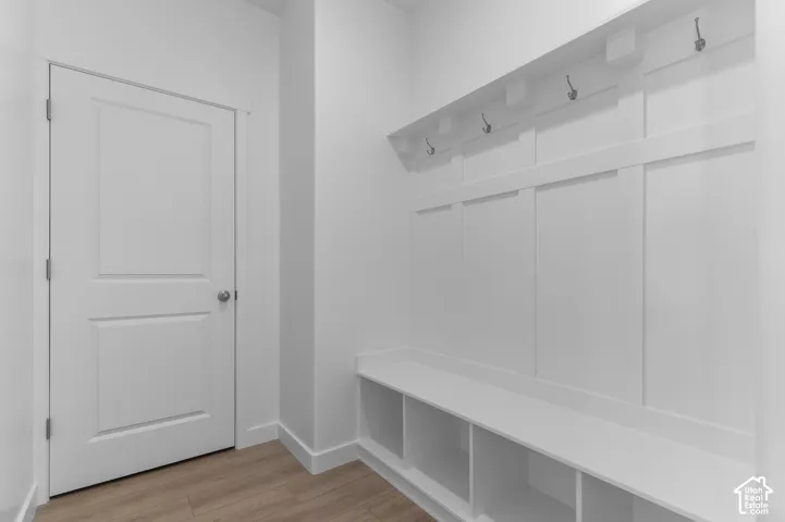 Built-in bench with cubby storage, white paneled wall with coat hooks, and light wood-finish flooring