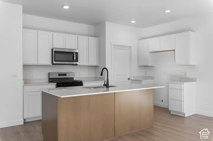Contemporary kitchen with white cabinetry, stainless steel microwave, gas range, wood-finish flooring, and a kitchen island with an integrated sink and matte black faucet