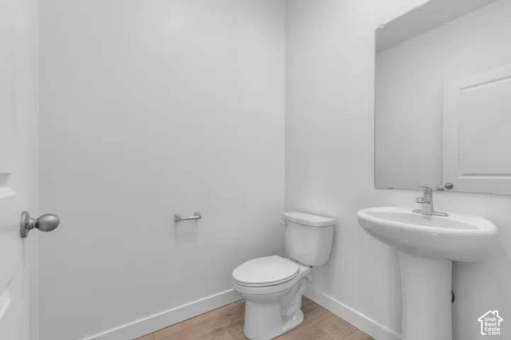 Pedestal sink with chrome faucet, wall-mounted mirror, and wood-finish flooring