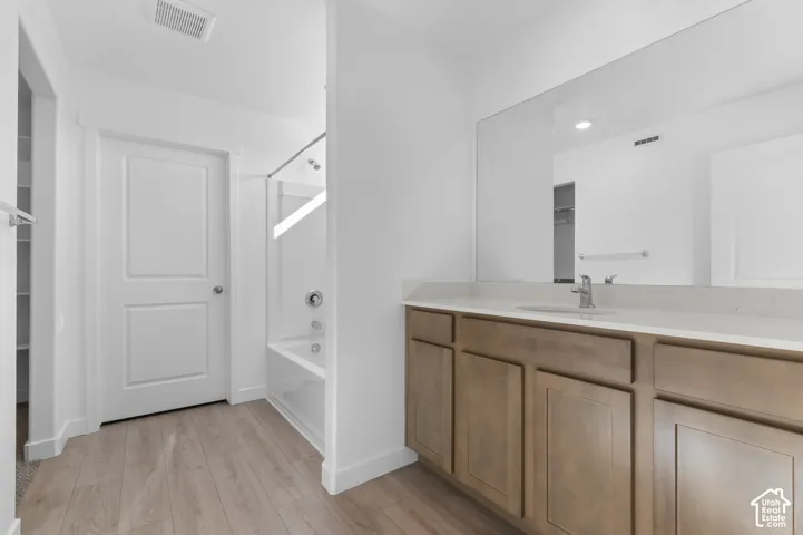 Wood-finish flooring with a light wood vanity, white countertop, and an integrated sink