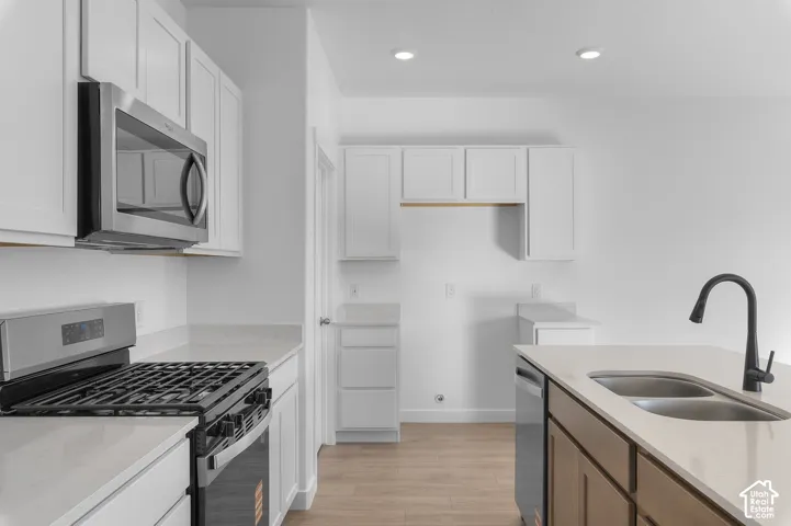 White shaker cabinetry with stainless steel appliances, light-toned countertops, and wood-finish flooring