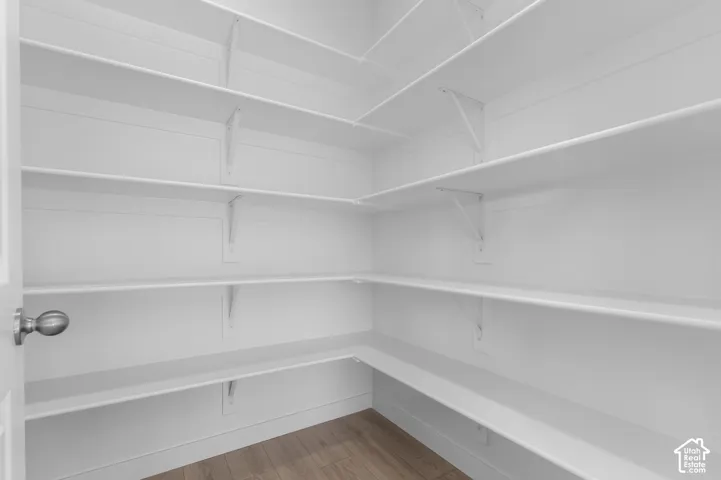 Walk-in pantry featuring extensive white shelving, wood-finish flooring, and a brushed nickel doorknob
