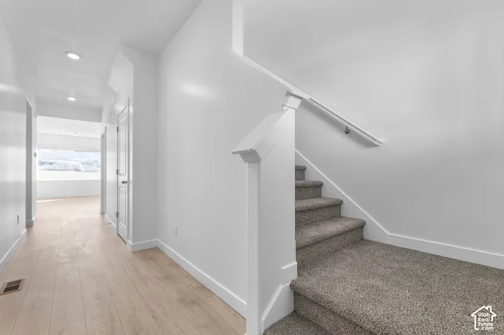 Carpeted staircase with white handrail, wood-finish flooring, recessed lighting, and white baseboards