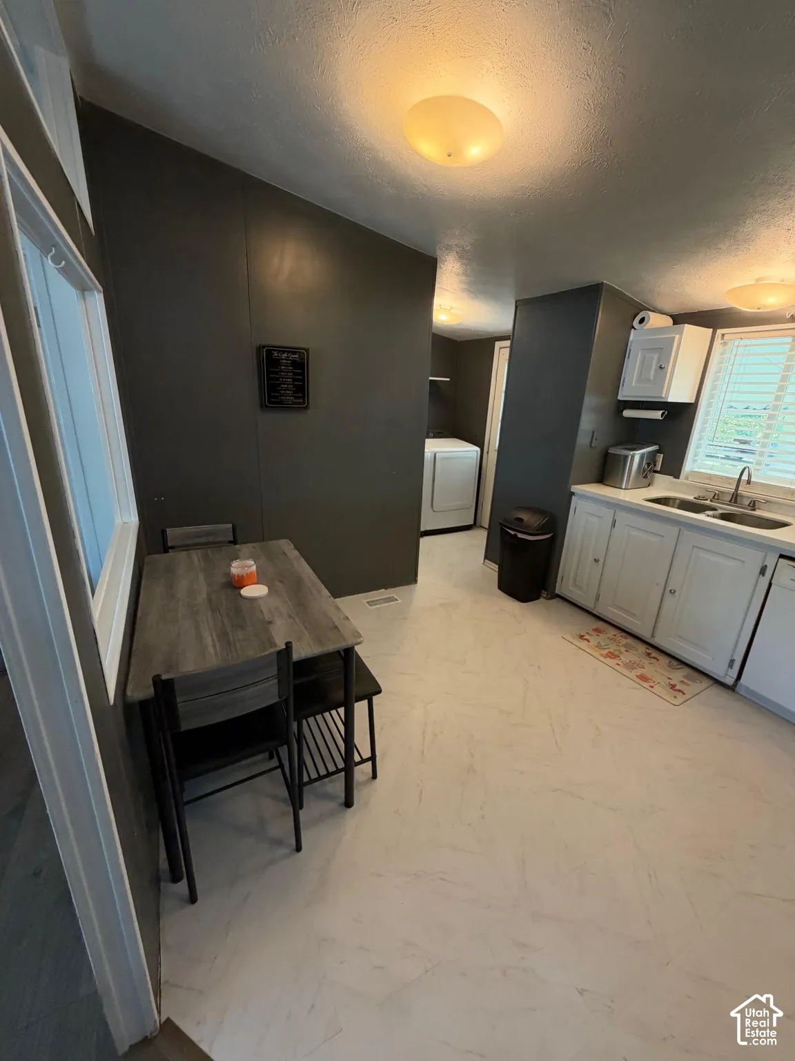Integrated kitchen and dining area featuring light-toned flooring, white cabinetry, and a window with blinds