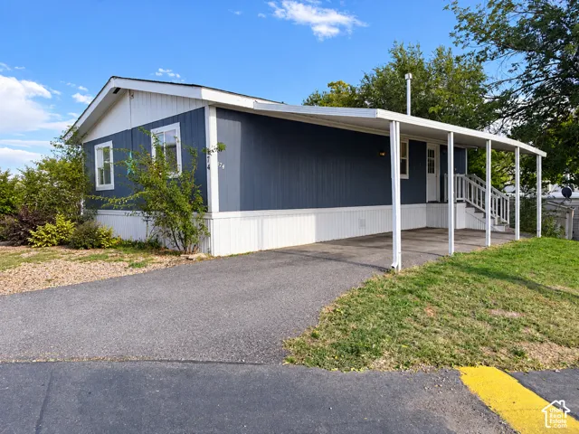 Exterior featuring blue siding, white trim, a covered carport, and a paved driveway