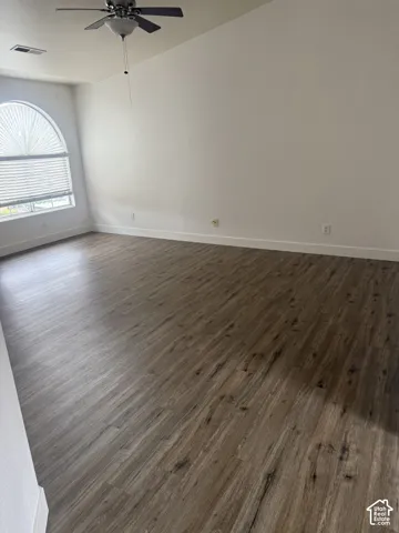 Vaulted ceilings, wood-finish flooring, and arched window with integrated blinds, complemented by a ceiling fan