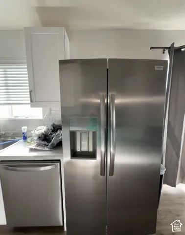 Stainless steel side-by-side refrigerator, integrated water and ice dispenser, stainless steel dishwasher, white shaker-style cabinetry, and white tile backsplash