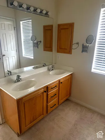 Dual-sink vanity with solid-surface countertop and integrated basins, complemented by wood cabinetry, a large wall-mounted mirror, and multi-bulb vanity lighting