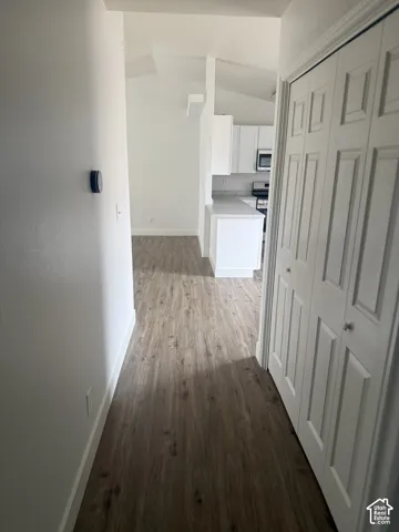 Interior hallway featuring wood-finish flooring, vaulted ceilings, white cabinetry, and dual-panel closet doors