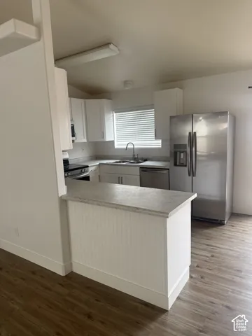 Kitchen featuring white cabinetry, stone-finish countertops, stainless steel appliances, a double-basin sink, and wood-finish flooring