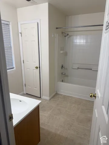 Bathroom featuring a shower and tub combination with a tiled surround, a vanity with a white countertop and integrated sink, and tile flooring