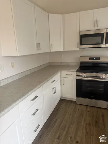 Kitchen featuring white shaker-style cabinetry, neutral stone-finish countertops, stainless steel appliances, and wood-finish flooring