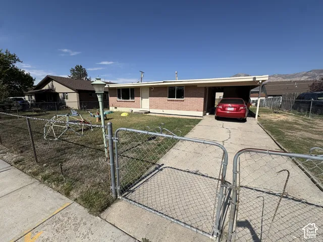 Brick exterior with a covered carport, chain-link fencing, and a paved driveway