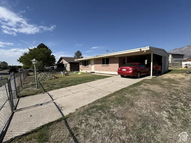 Red brick exterior with a covered carport, paved driveway, and chain-link fencing