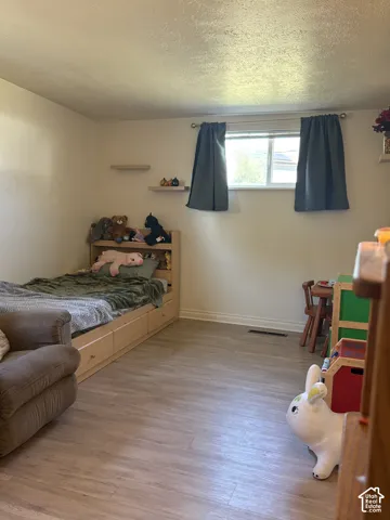 Room with wood-finish flooring, two wall-mounted shelves, and a window with curtains